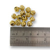 A collection of gold metallic jingle bells with a ruler for scale on a white background